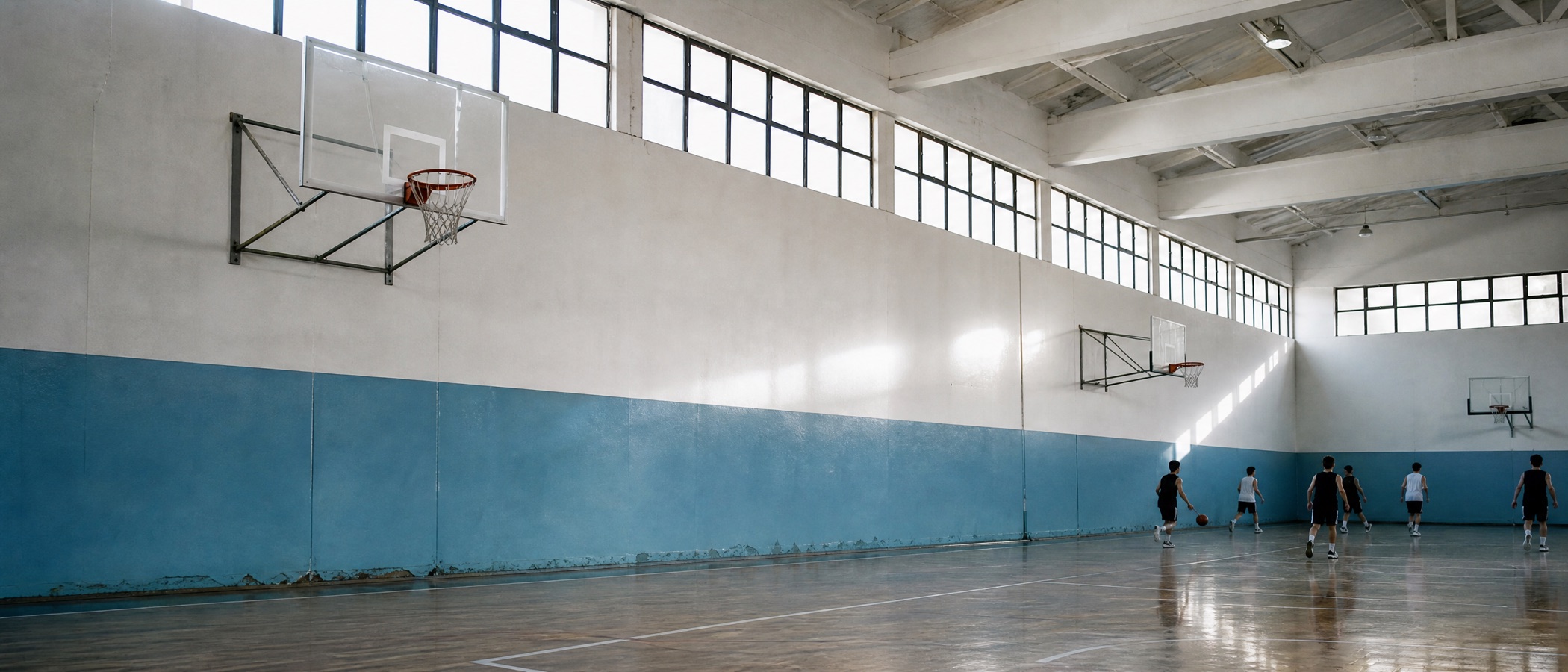 Spor salonunda yan yana basketbol potaları, uzakta ısınan birkaç oyuncu